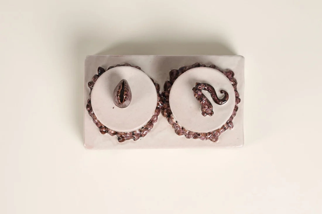 A pair of handmade oval stud earrings with white centers, dark red beaded borders, and dark red teardrop and scroll charms, displayed on a rectangular white backing against a light beige background.
