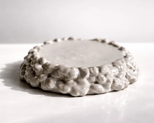 A small round ceramic tray with a textured, bubble-like raised rim, shown on a plain white surface with a soft shadow.