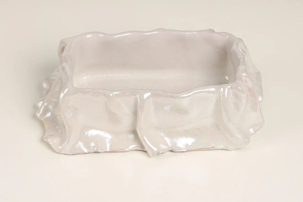 A small, rectangular ceramic dish with a wavy, ruffled rim and a glossy, iridescent finish, photographed on a plain off-white background.