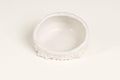 A small white ceramic dish with a textured, scalloped rim, photographed on a seamless white background.