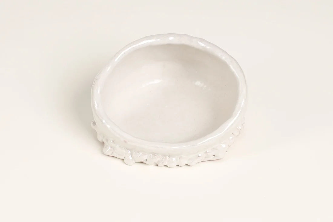 A small white ceramic dish with a textured, scalloped rim, photographed on a seamless white background.