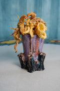 A ceramic food holder shaped like a tree trunk, filled with golden-brown fried calamari rings on skewers, set against a textured blue background.
